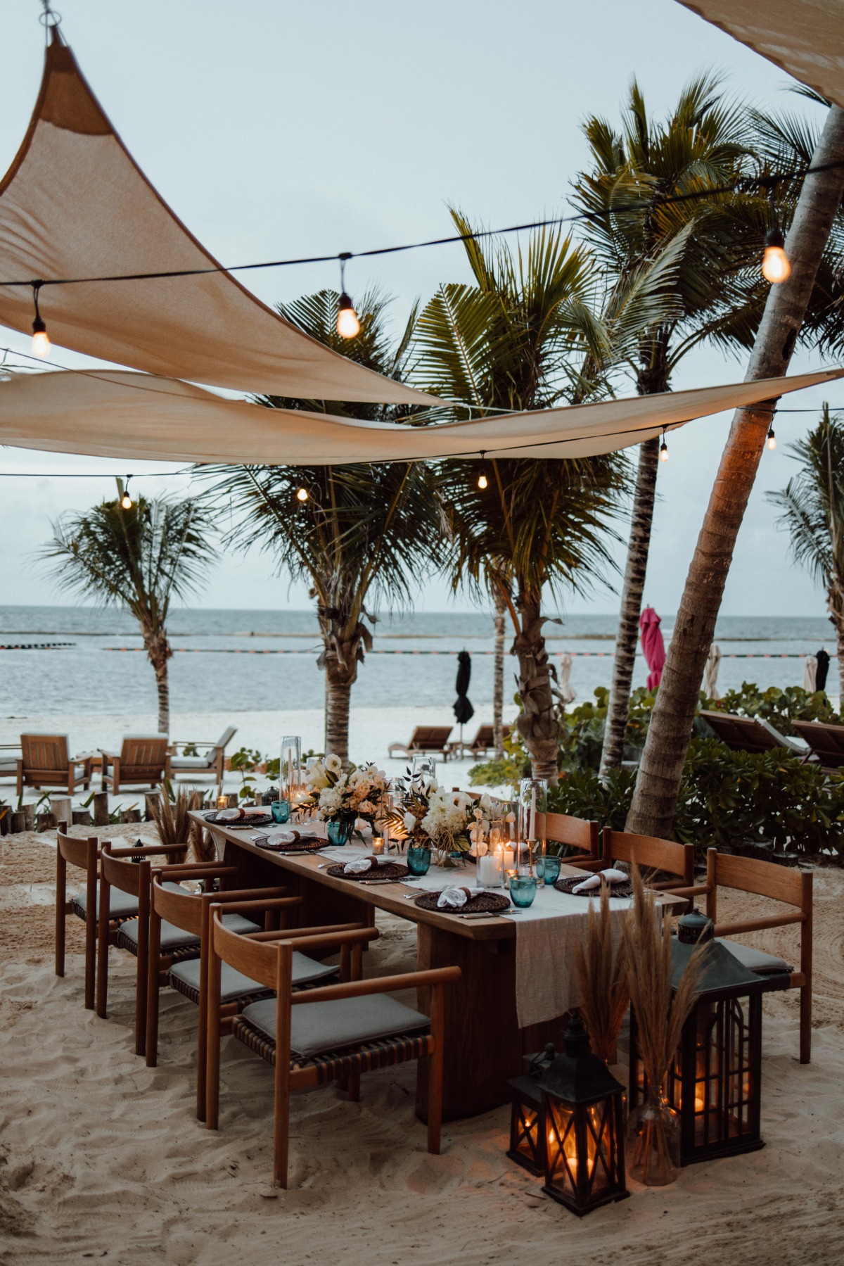 Reception space with tables, palm trees, awnings, and centerpieces next to beach
