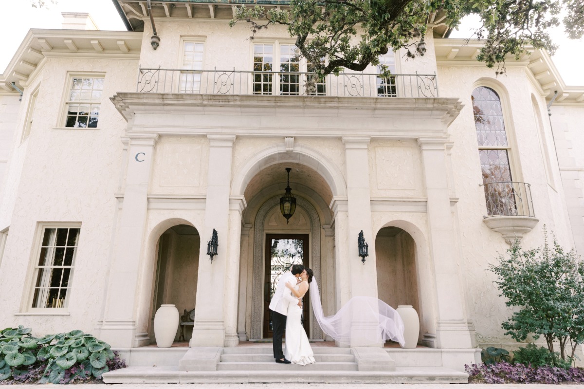 Bride and groom kissing on steps with veil flowing behind her