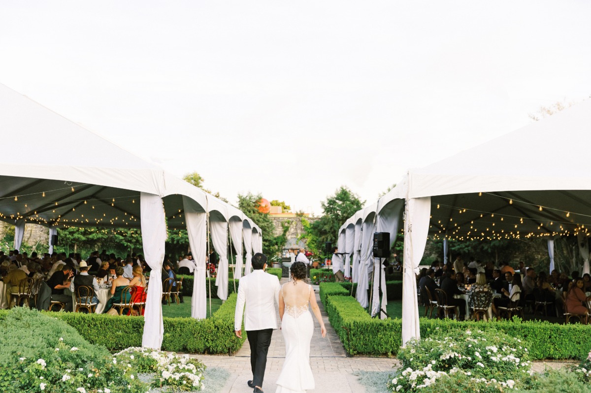 Bride and groom walking into tented reception with string lights