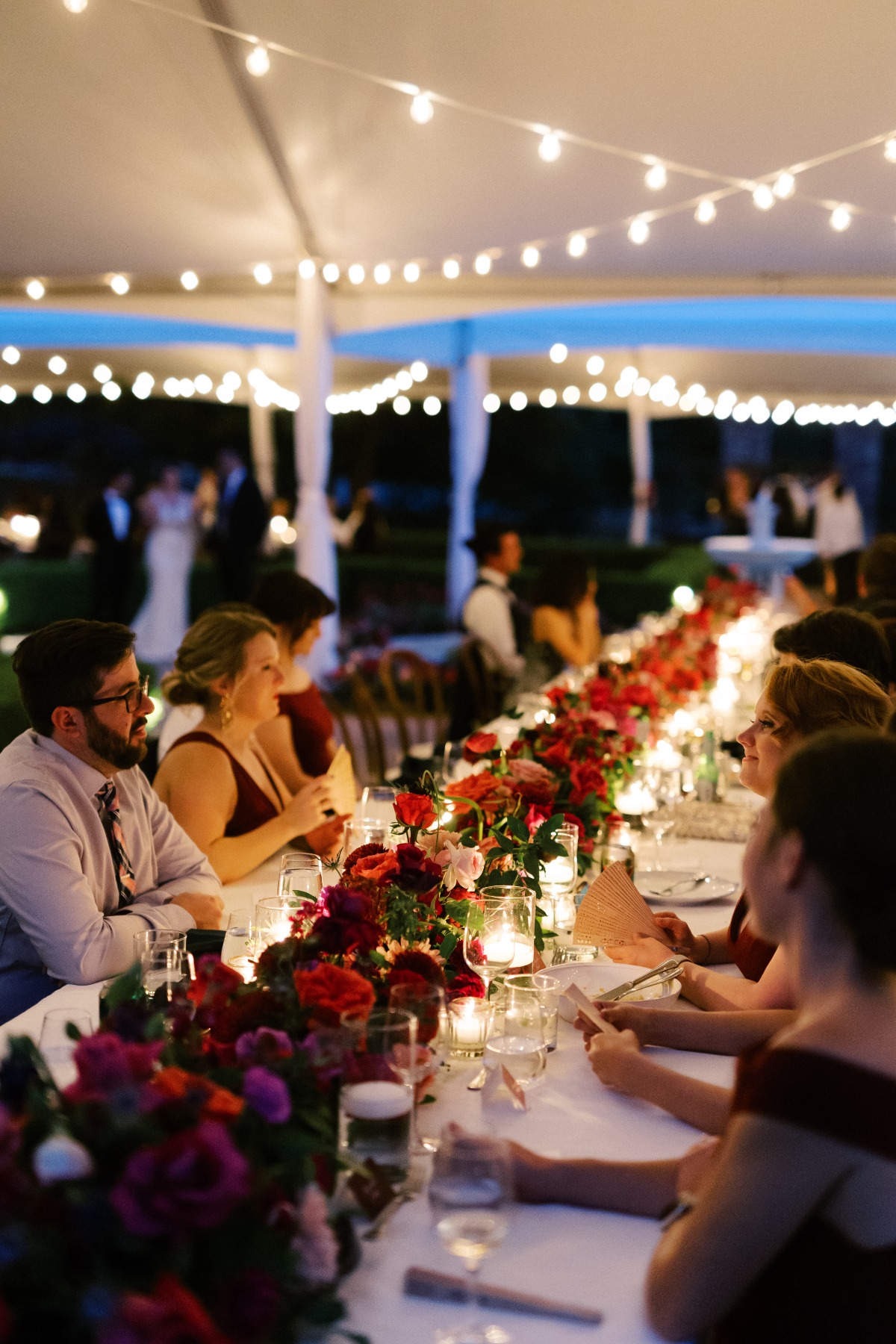 Guests at reception at night under string lights with lit candles and floral table runner