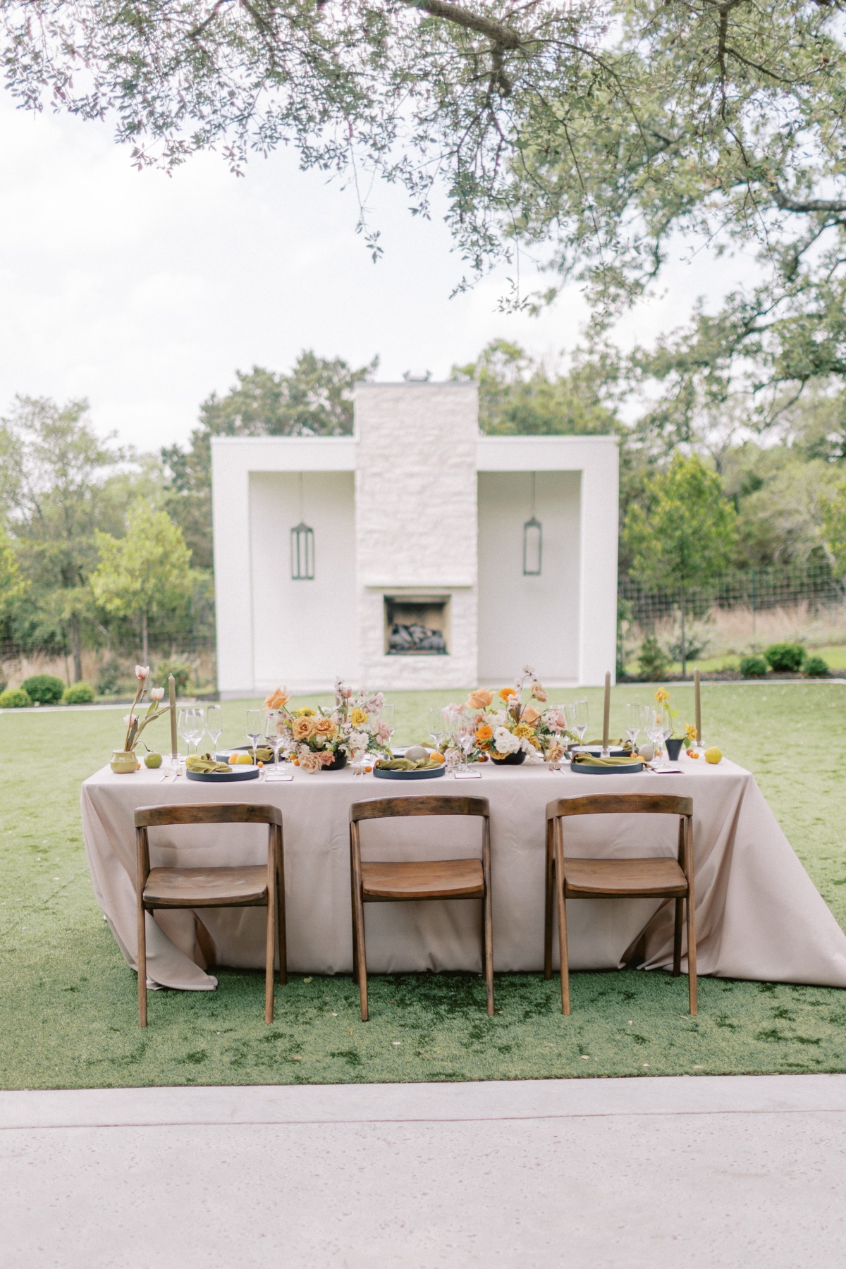 Reception table with place settings and summer floral centerpieces in front of outdoor fireplace