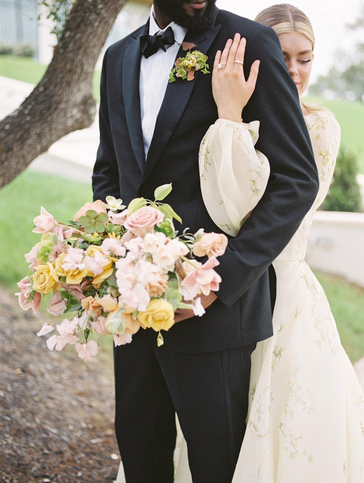 Bride hugging groom from behind while groom holds bouquet