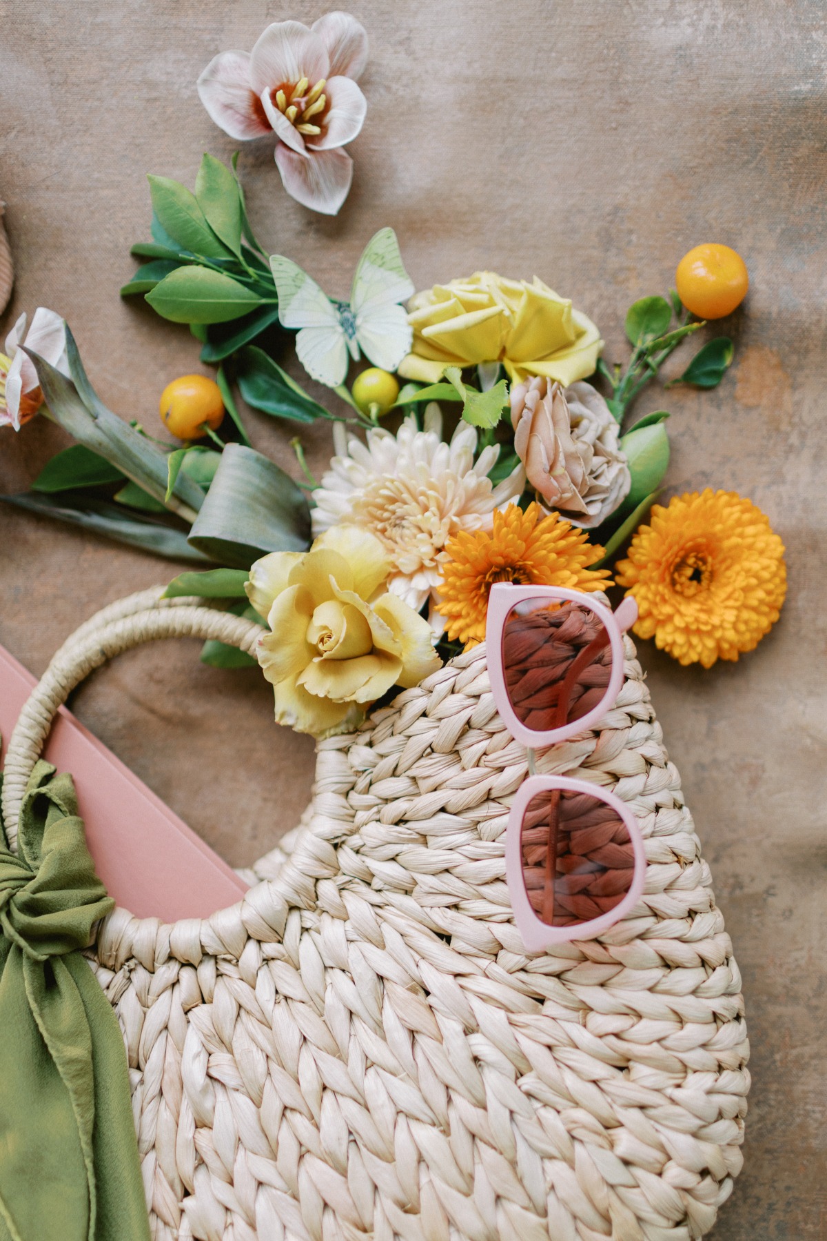 Aerial view of rattan handbag, pink sunglasses, and flowers with butterflies