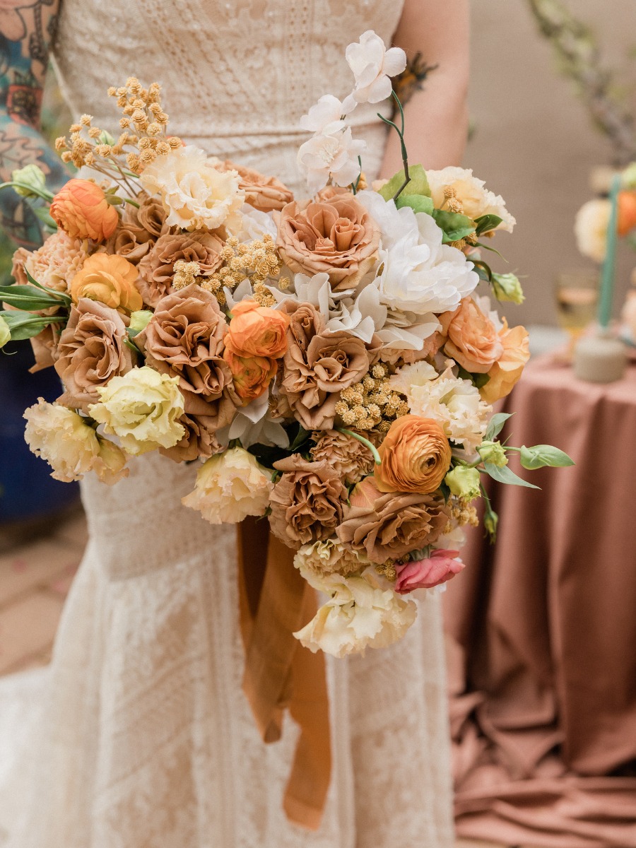 Bride holds rustic orange and beige wedding bouquet