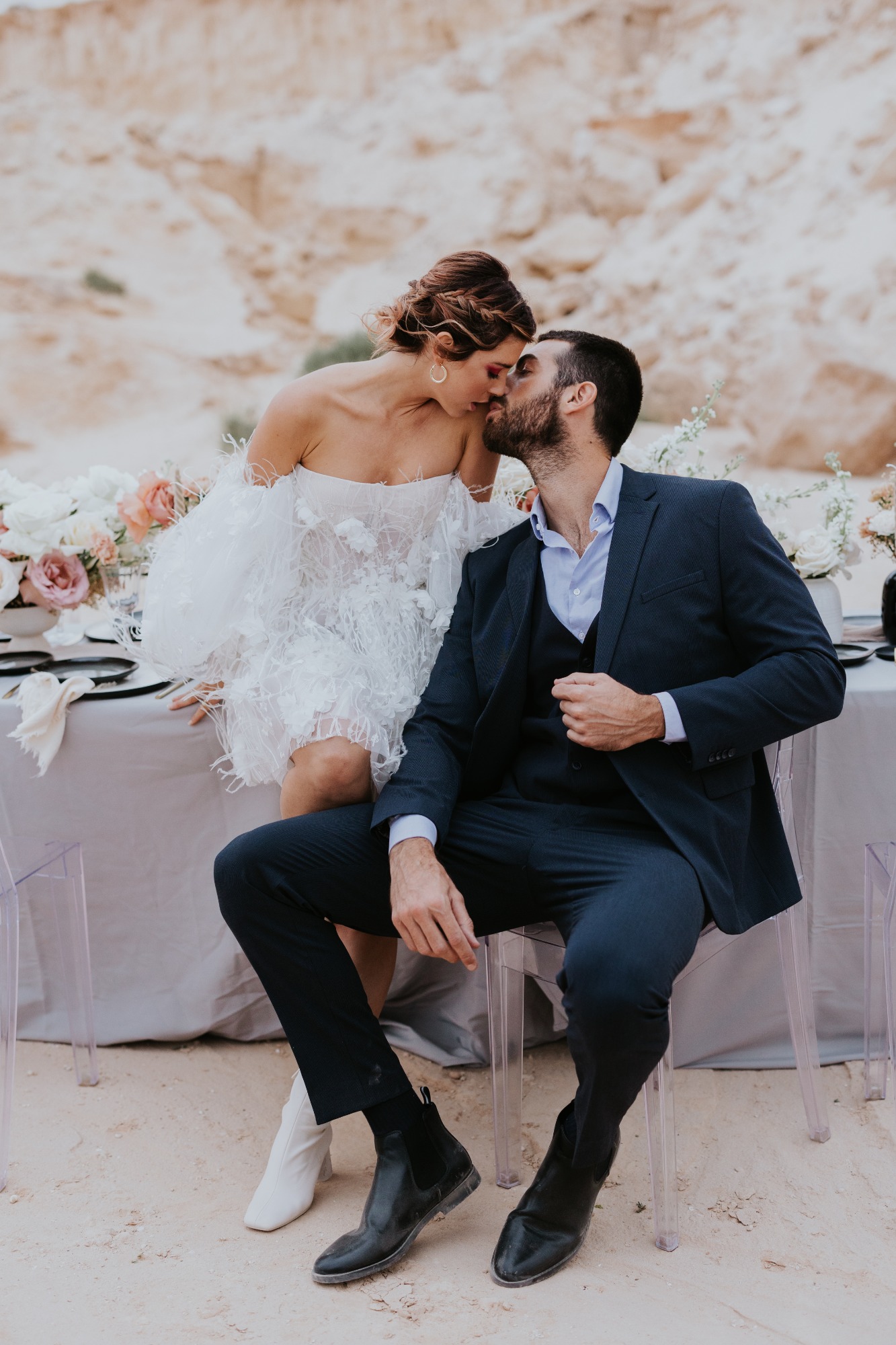 bride and groom share a kiss at their desert wedding table
