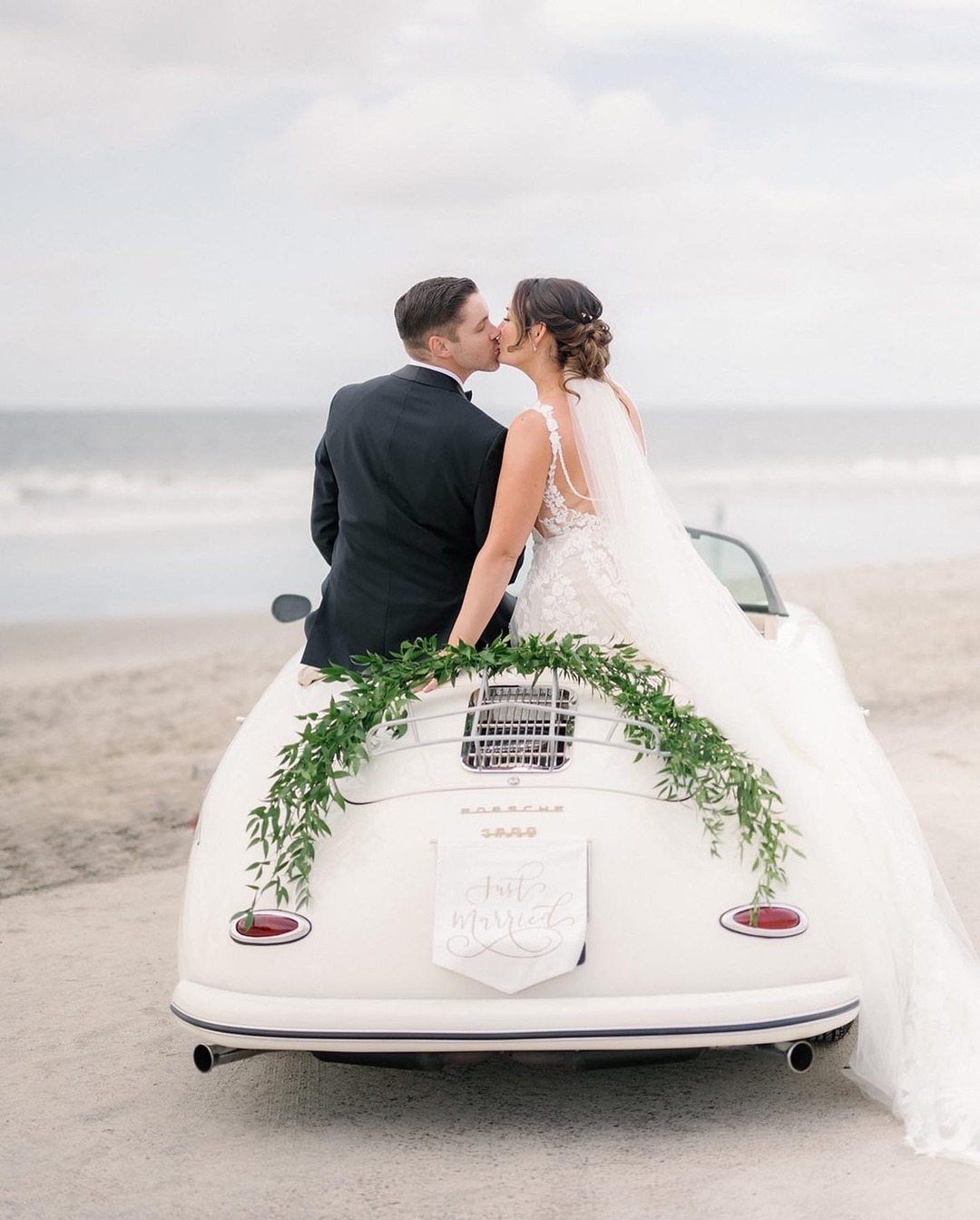 Newlyweds kissing in vintage Porsche on beach wedding day