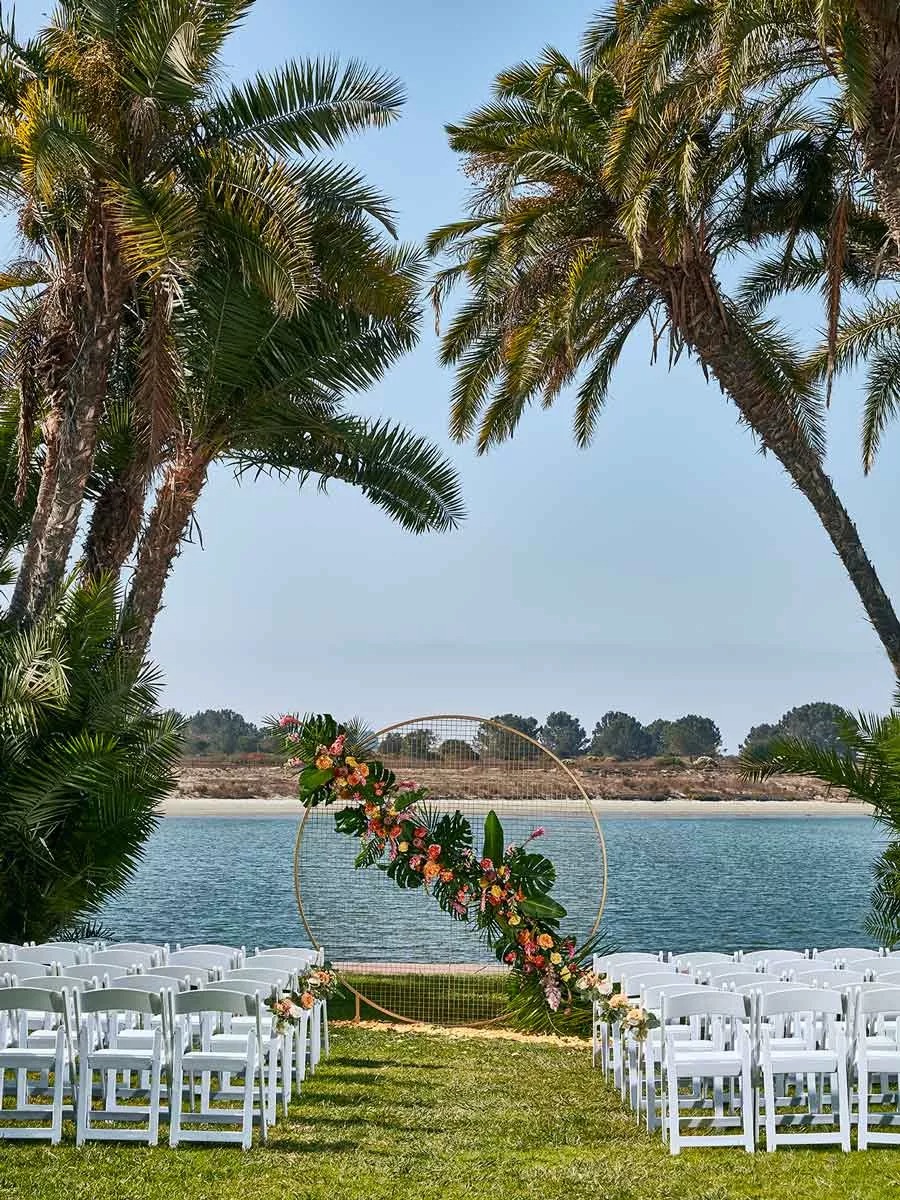 Wedding ceremony setup near the water with palm trees and floral decor