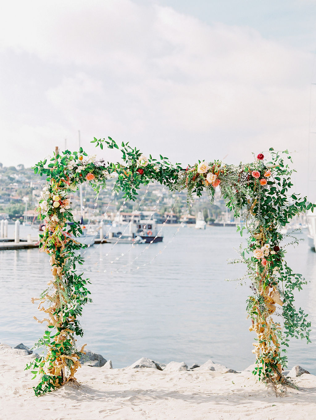 Beach wedding arch with floral greenery and harbor view