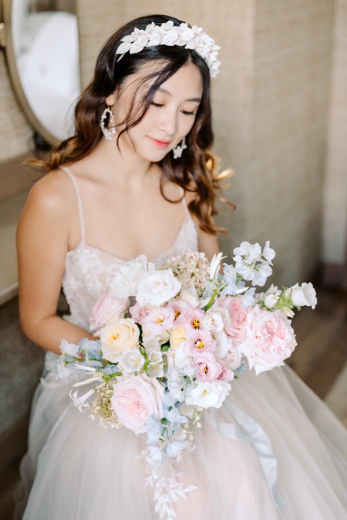 bride with white floral hatband with hair down in toussled waves holding blue and pink bouquet