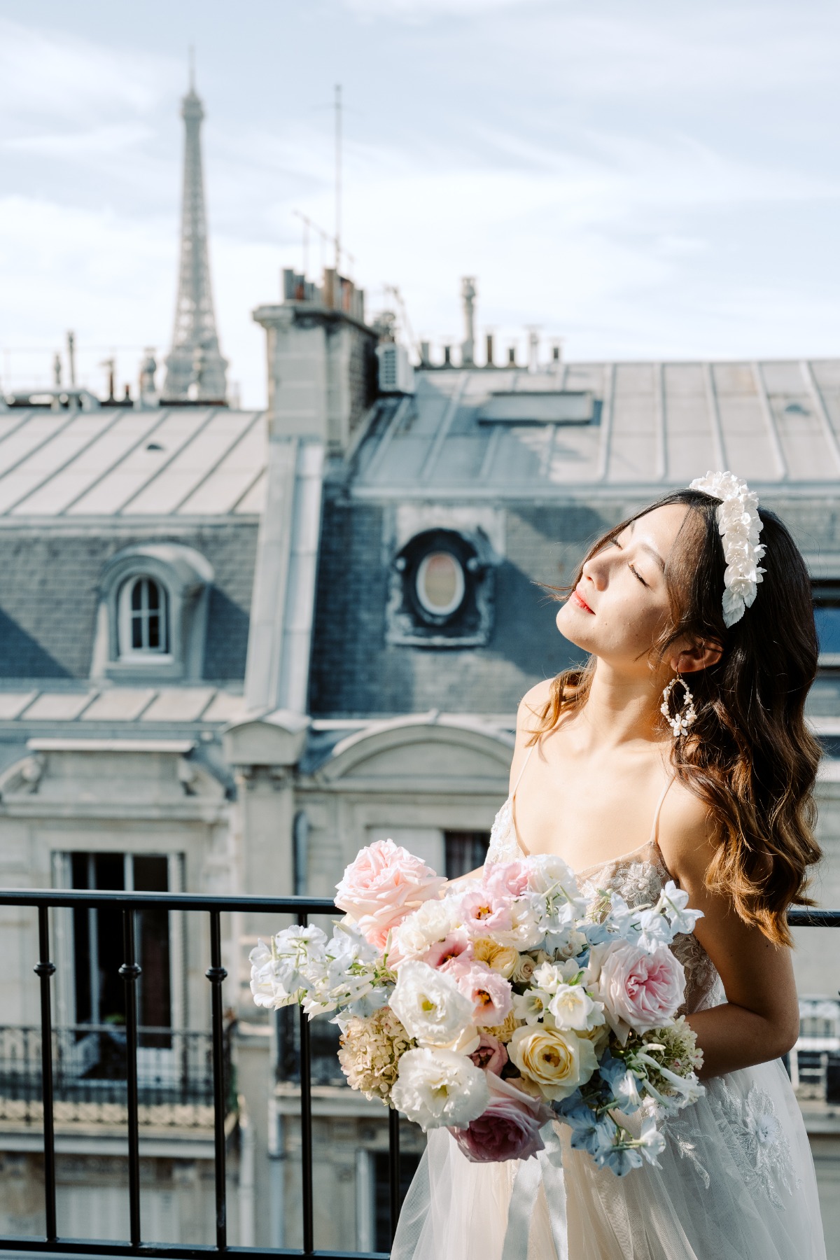 bride poses on balcony with bouquet with the Eiffel tower in the background