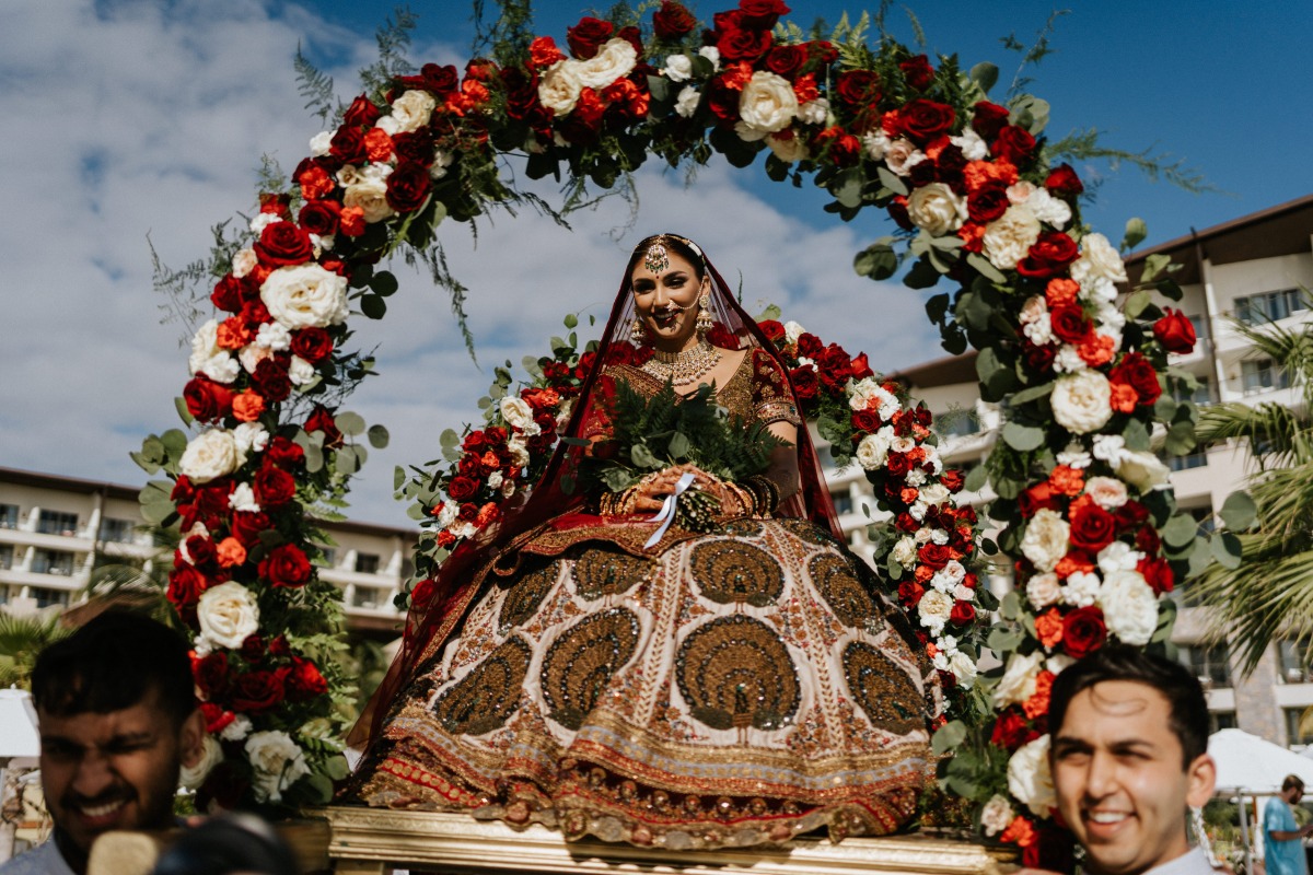 Indian bride being carried down the aisle with floral arch