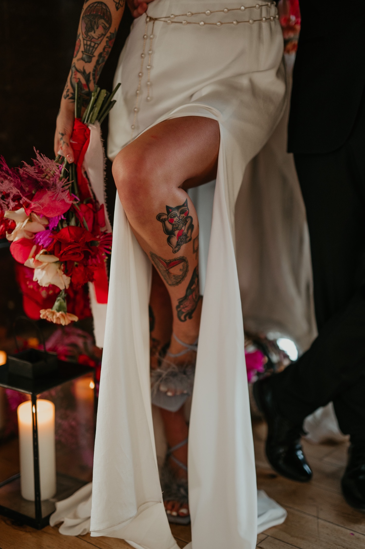 tattooed bride in fitted wedding gown with a slit carrying pink and red bouquet