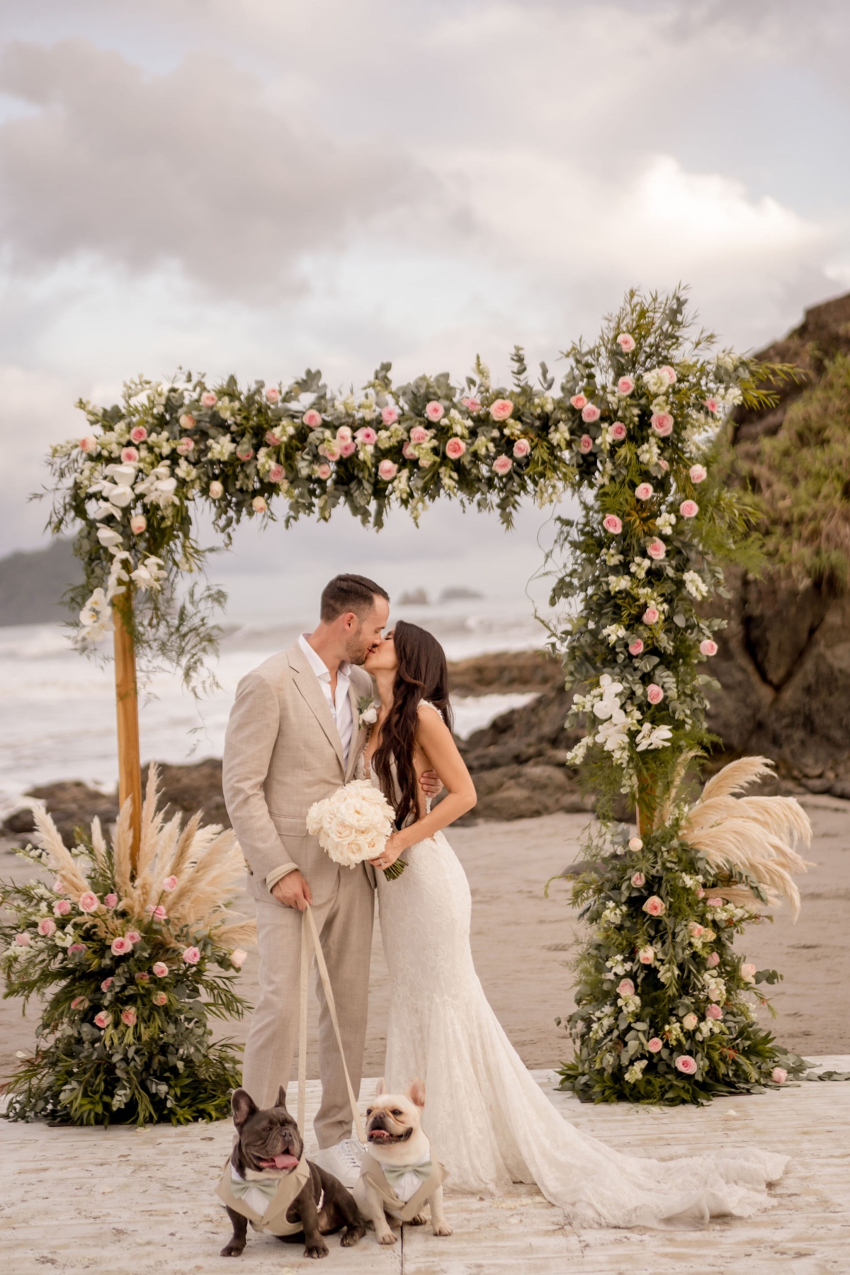 pink and green floral arch at beach wedding with French bulldogs
