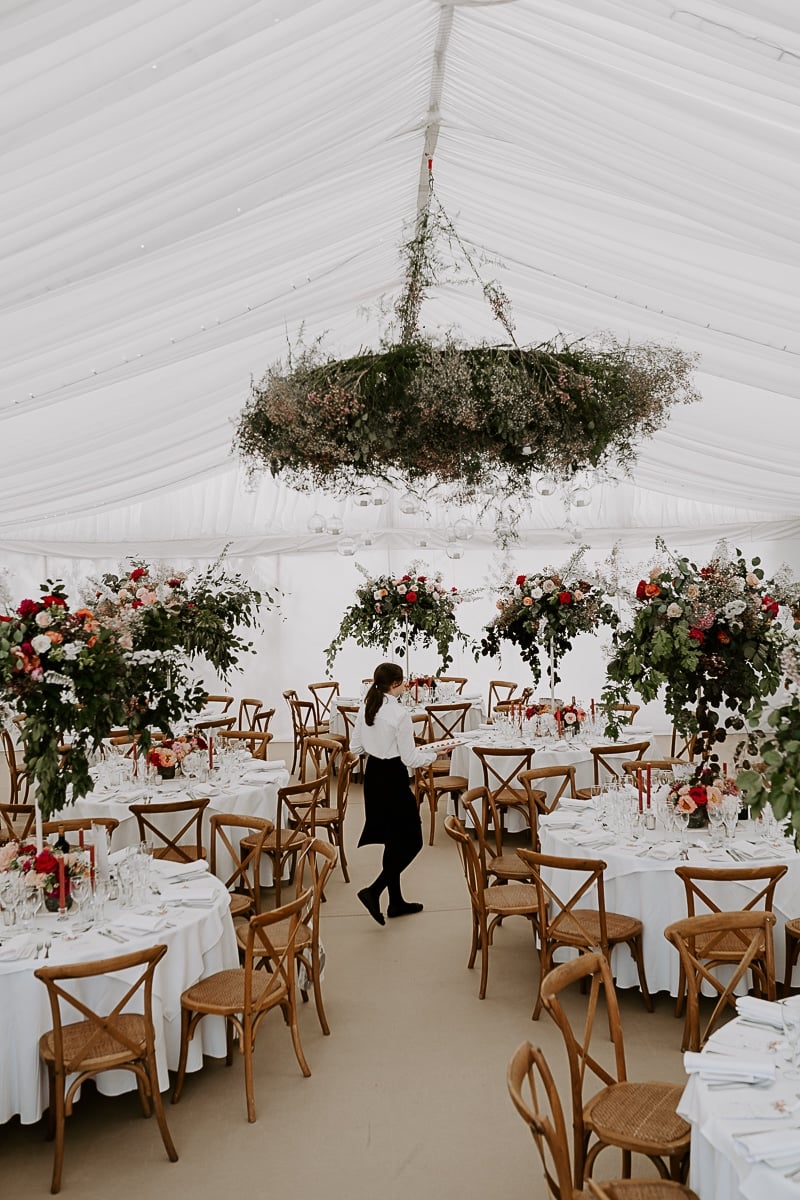 tented wedding reception with hanging floral installations and red and pink centerpieces