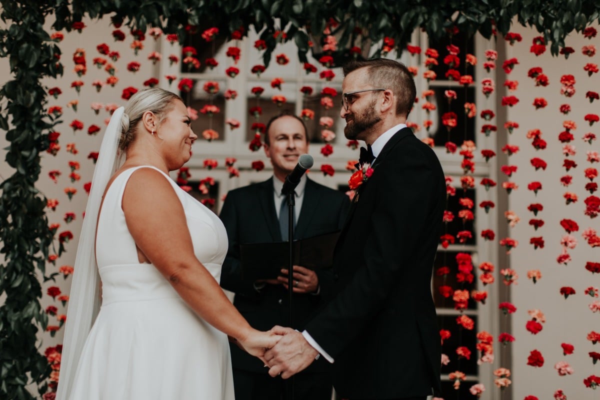 Modern wedding ceremony in front of floral wall 