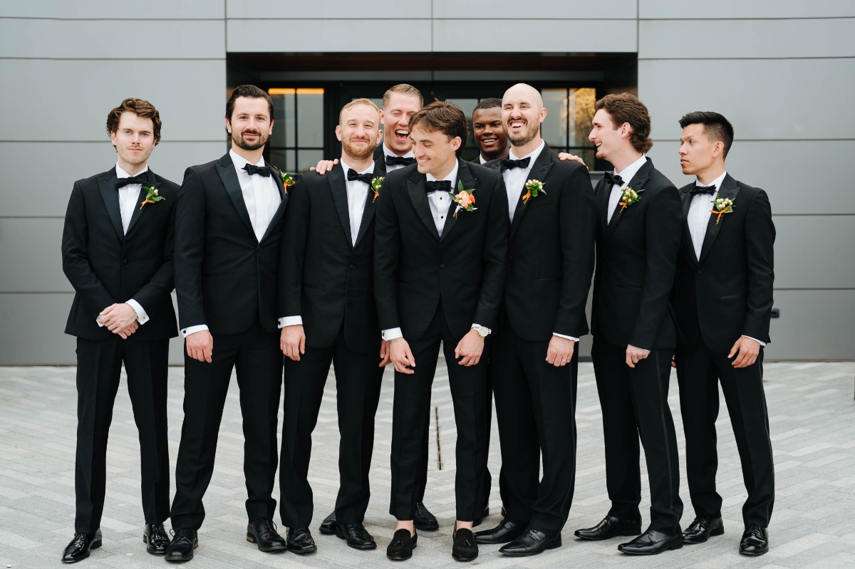 groom and groomsmen in black tuxes with orange flowers
