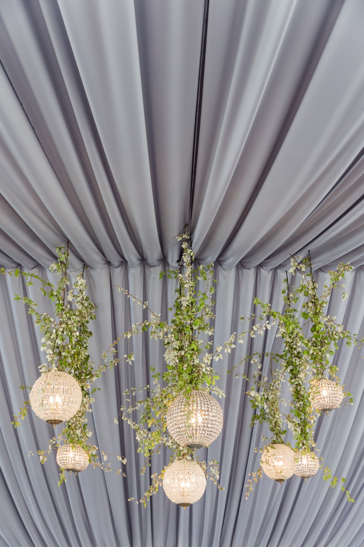 gray fabric draped reception with greenery and chandeliers 