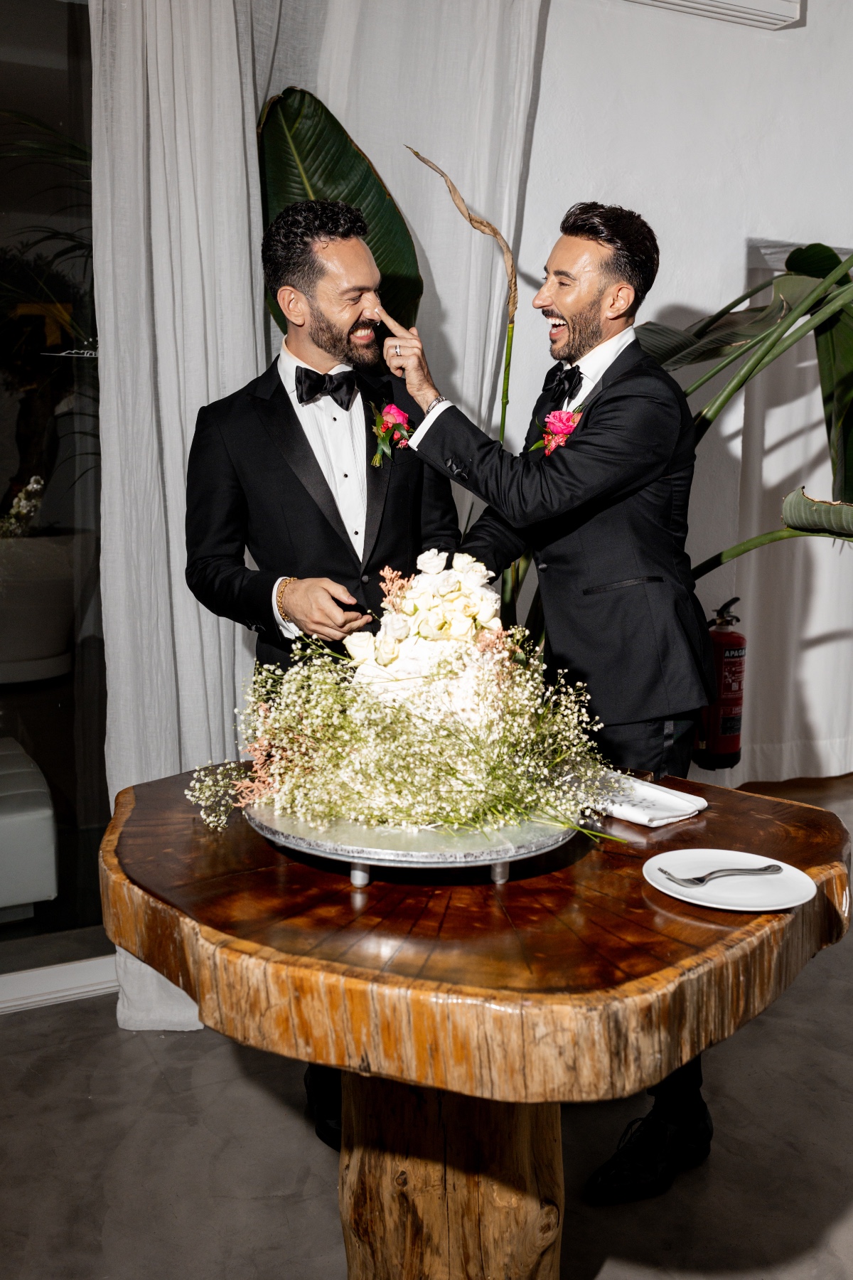 Playful grooms exchanging wedding cake frosting at floral table