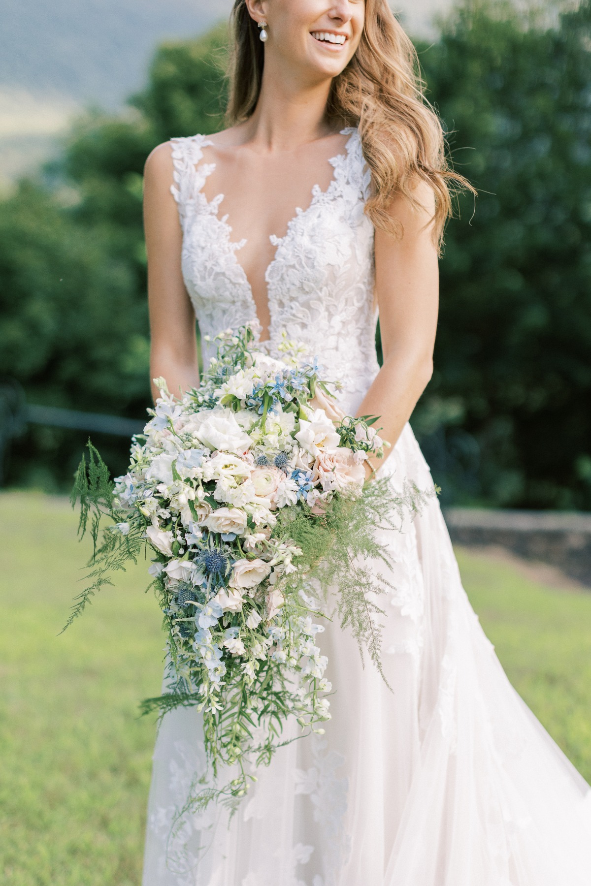 Bride in elegant floral gown carrying blue accented bouquet 