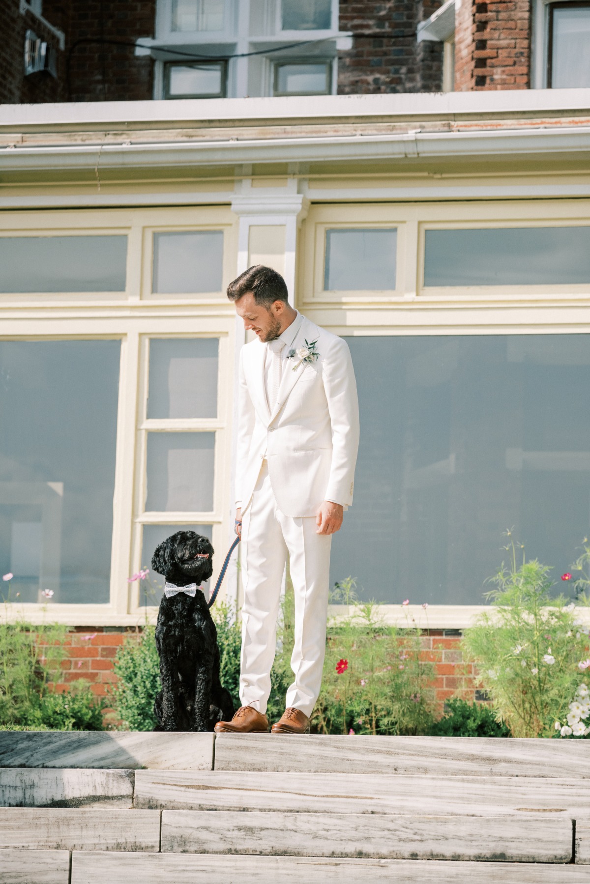 Groom in all white suit walking down aisle with his dog 