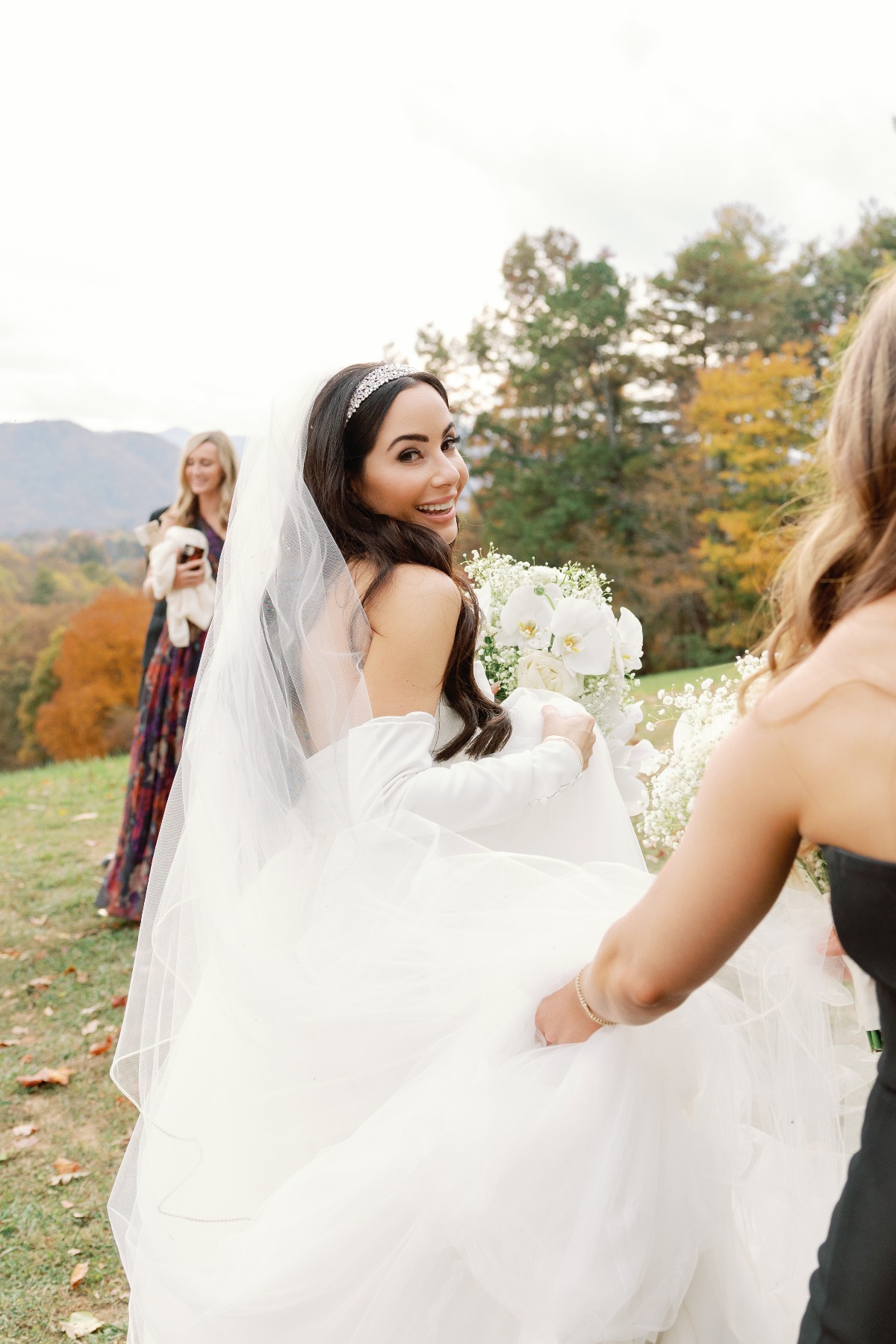 Bridesmaids helping bride carry gown to ceremony 