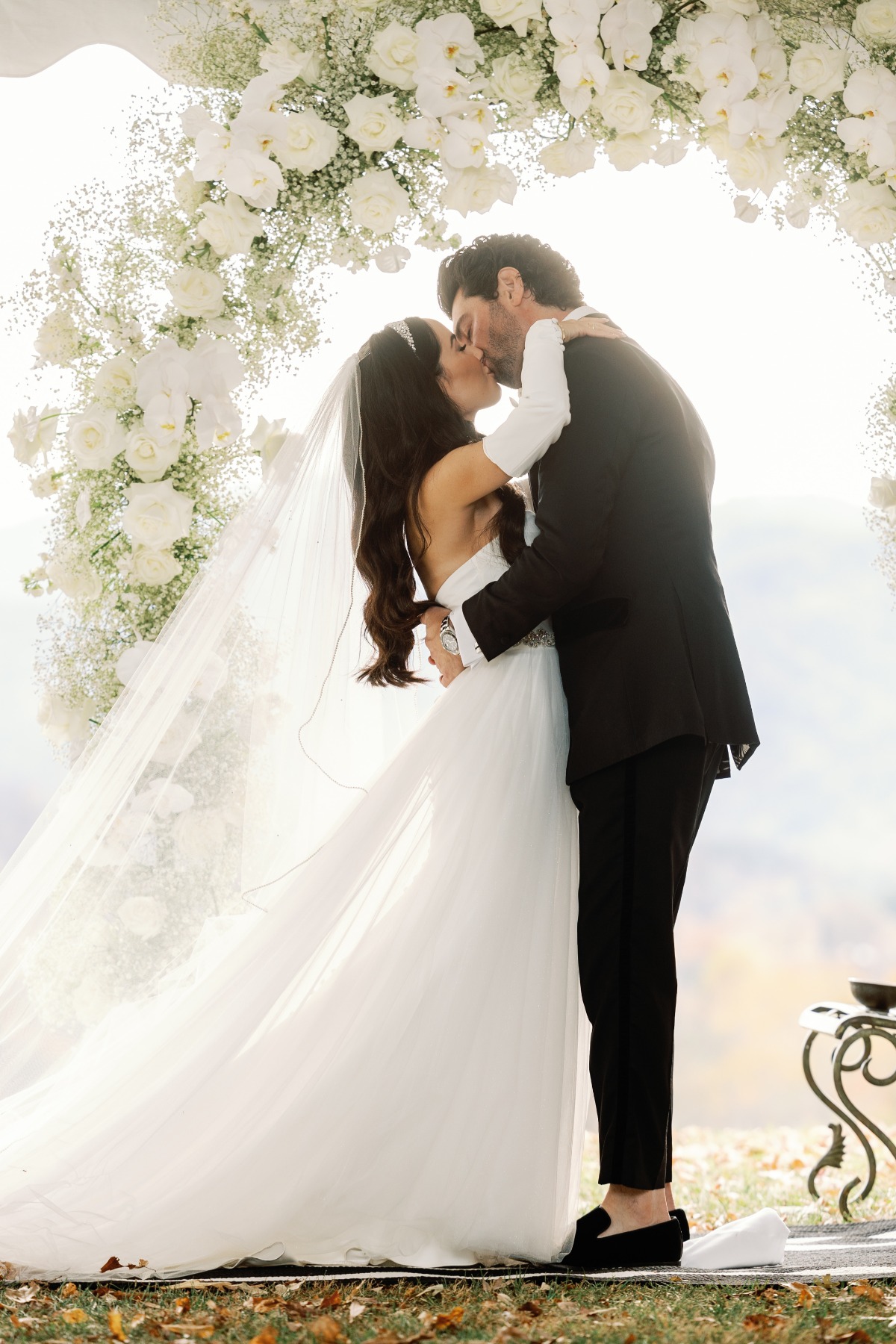Romantic first kiss under white rose and baby's breath arch 