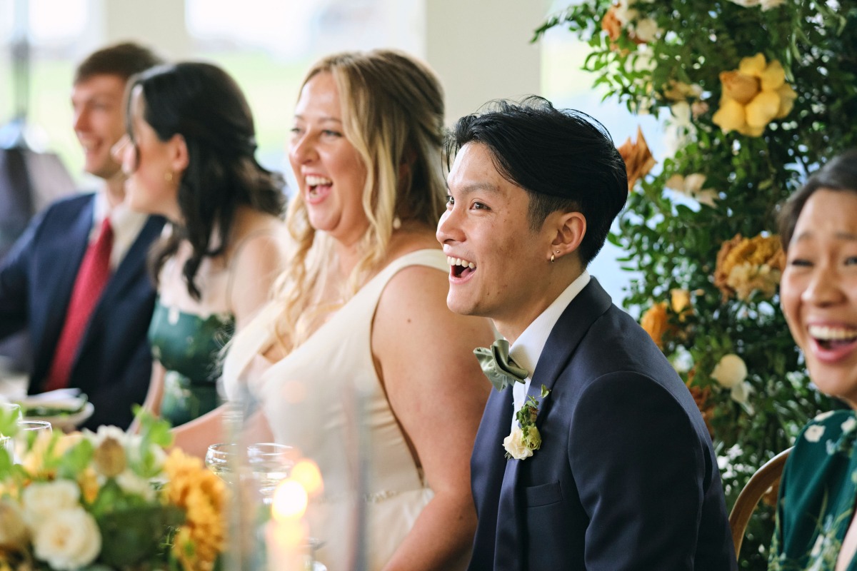 Joyful bride and groom laughing at reception toasts 