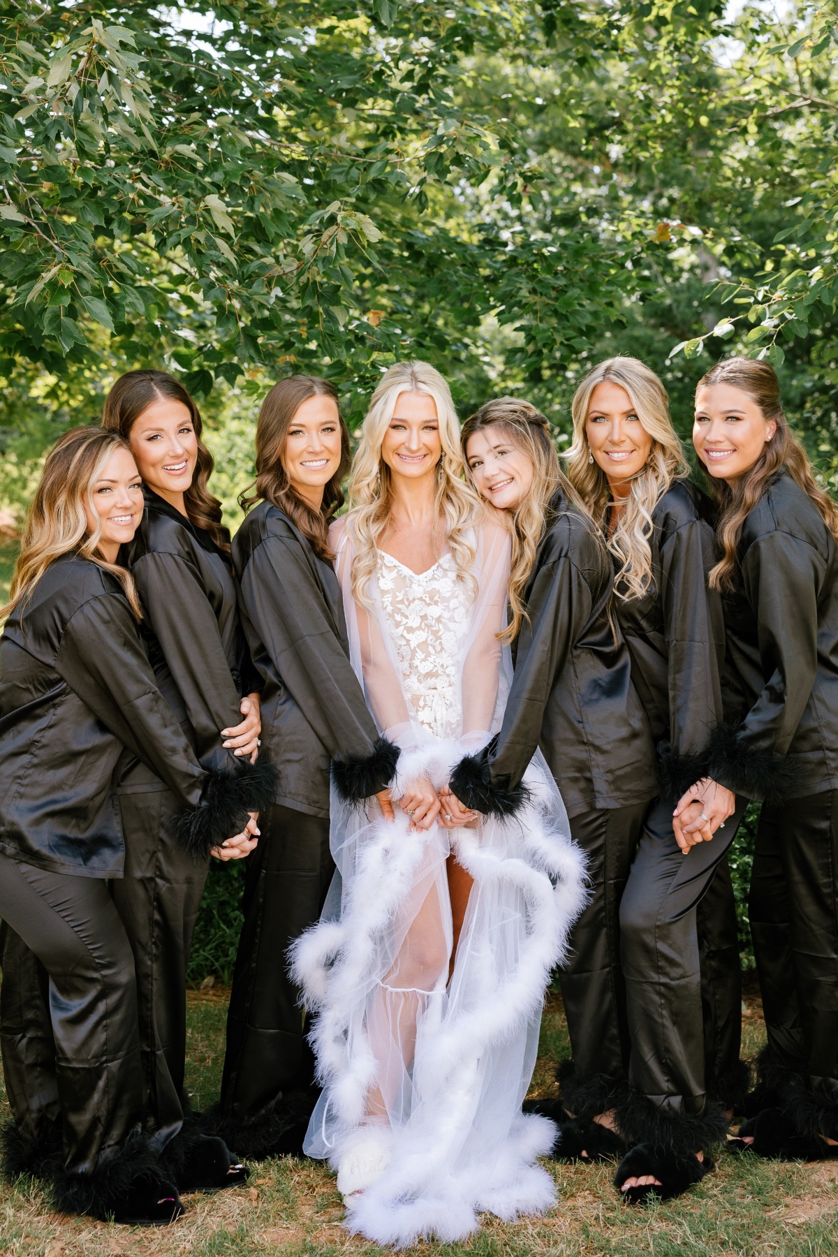 Bride in feathered robe with bridesmaids in black pajamas