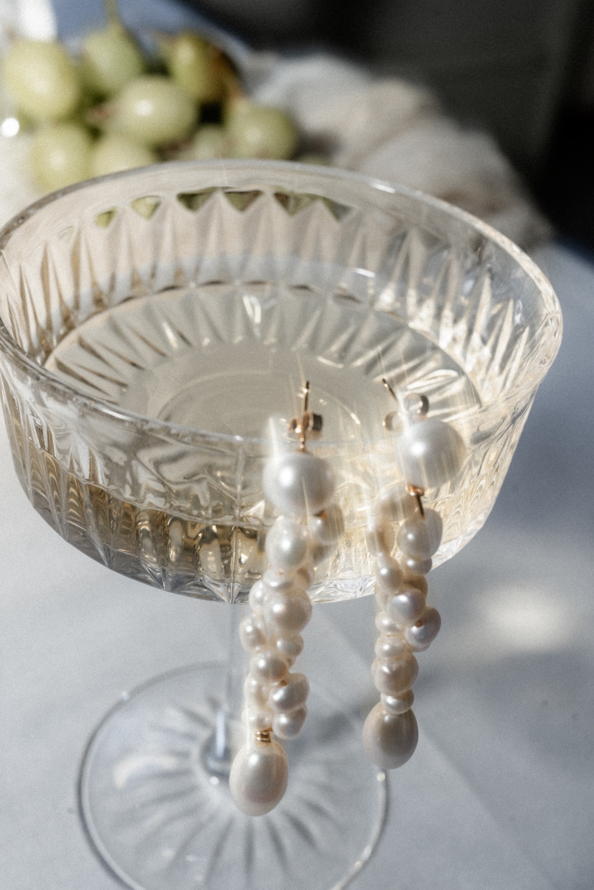 Luxurious pearl earrings resting on champagne goblet 
