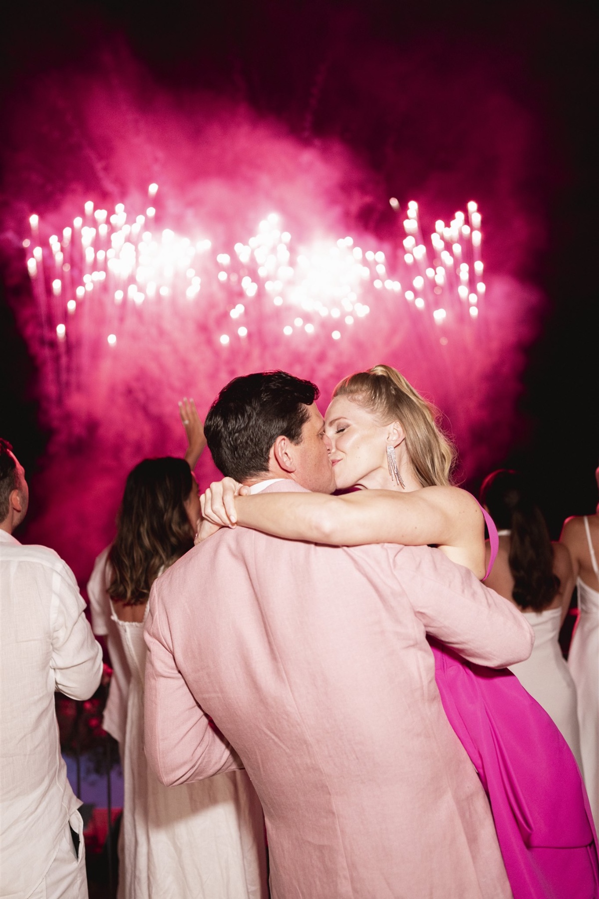 Bride and groom watching pink fireworks at welcome party 