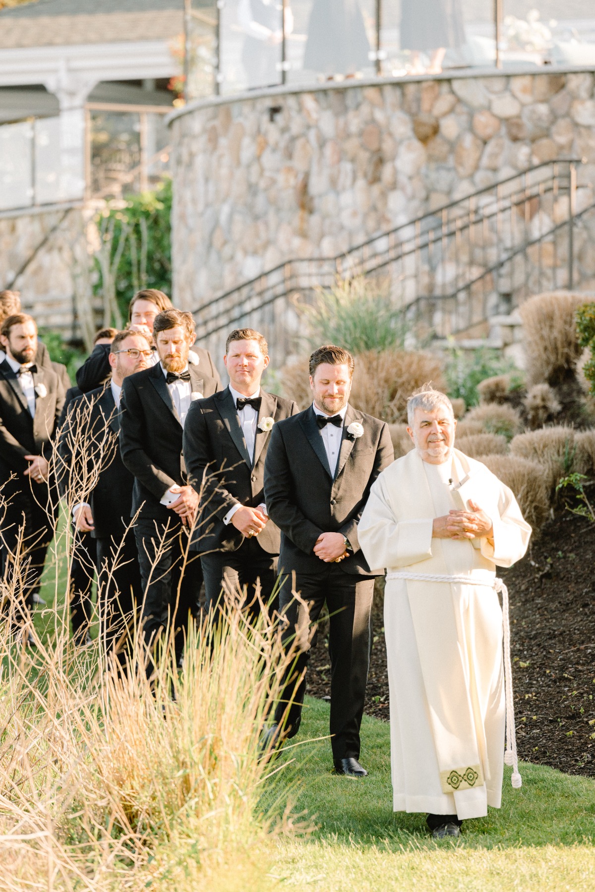 Priest leading groom and groomsmen into Cape Cod ceremony
