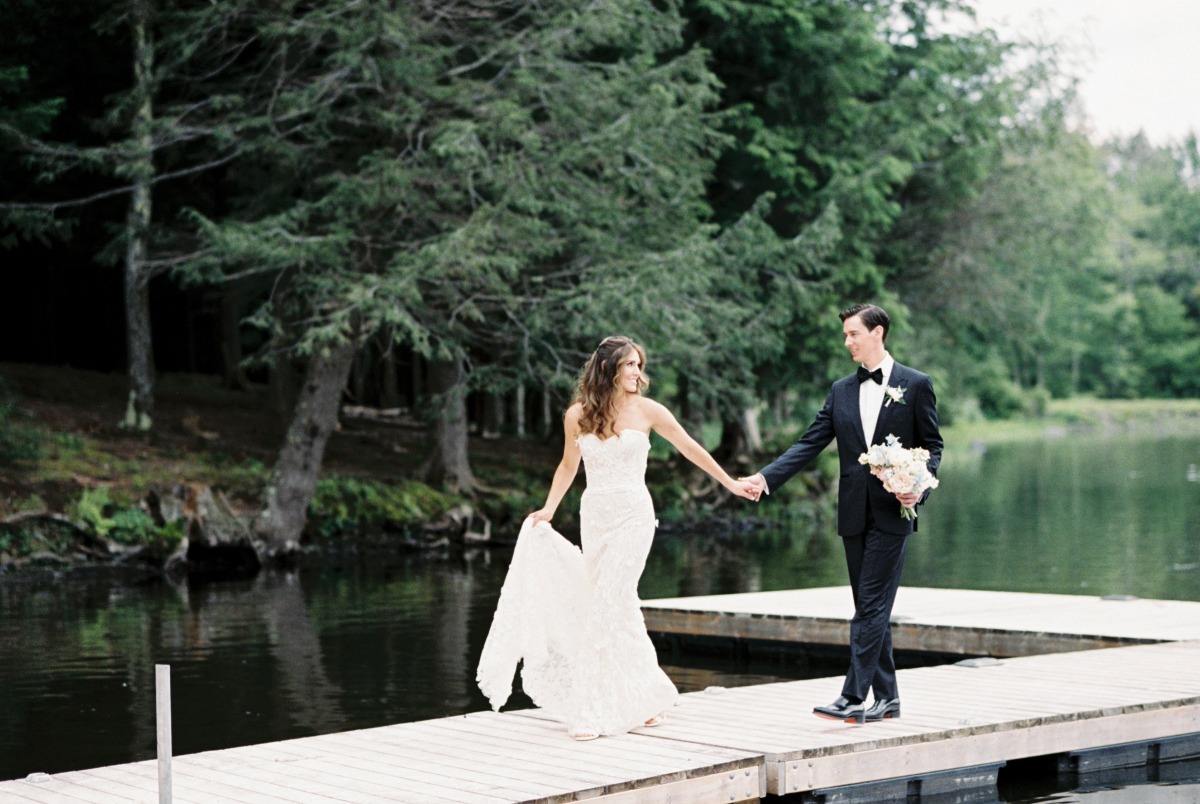 Bride leading groom down lake boat dock to reception 