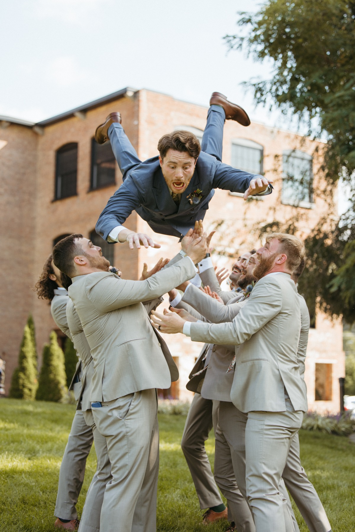 Playful groomsmen tossing groom into the air 