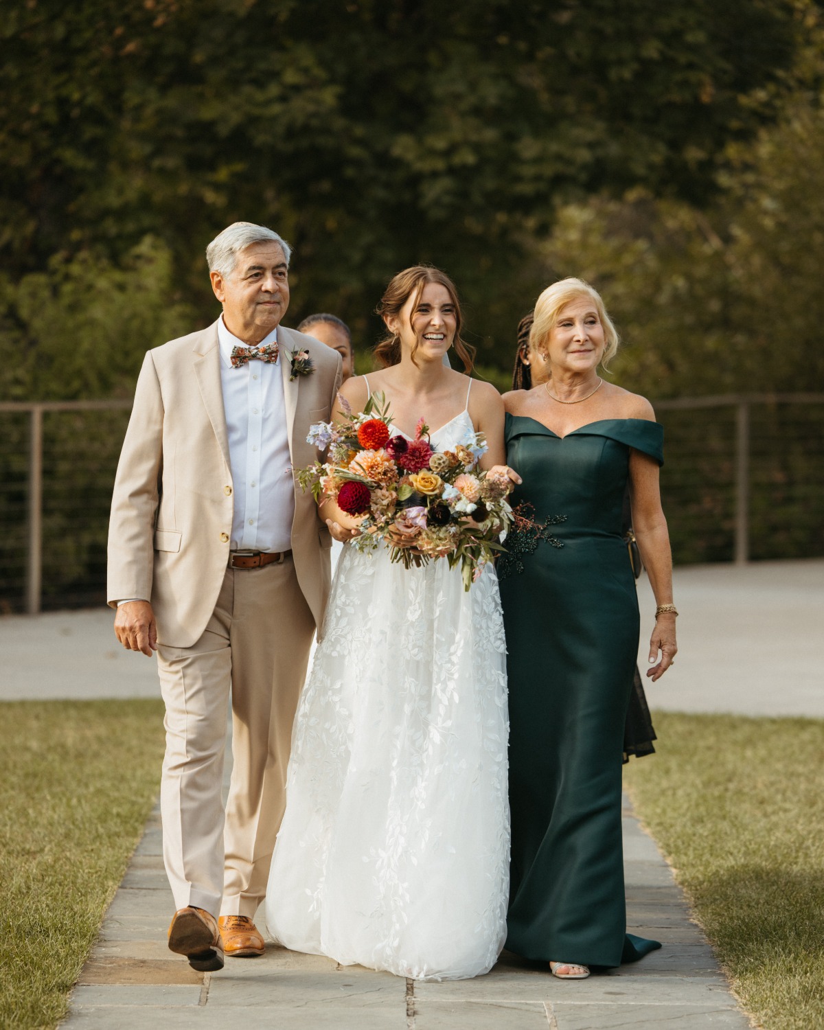 Emotional bride walking down aisle with elegant mother and father