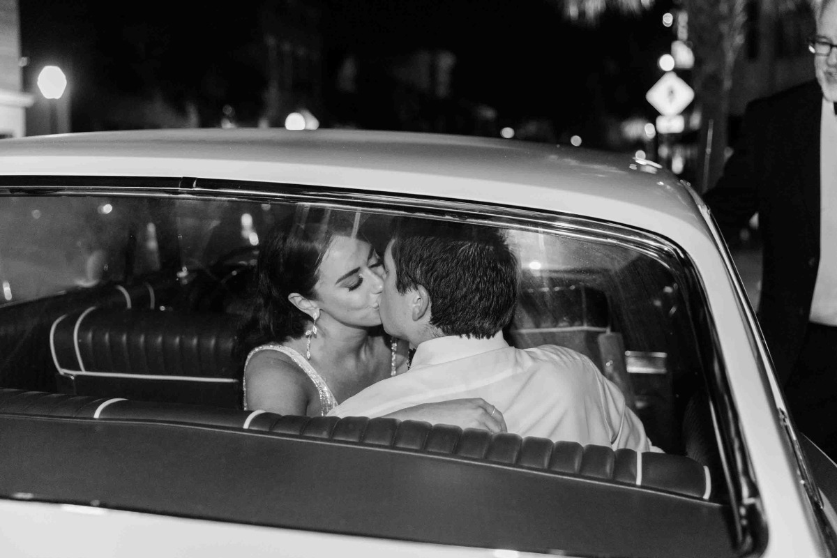 Bride and groom kiss in vintage family getaway car for honeymoon