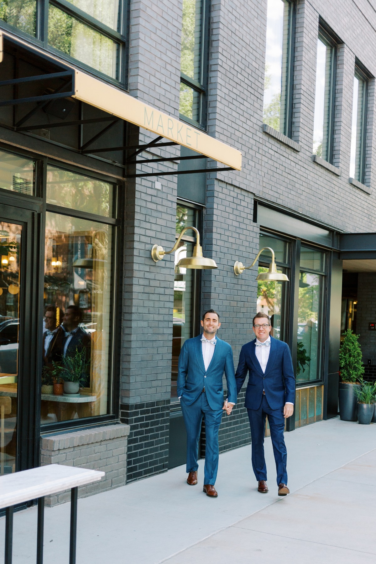 Two grooms in custom blue suits walking through Denver 