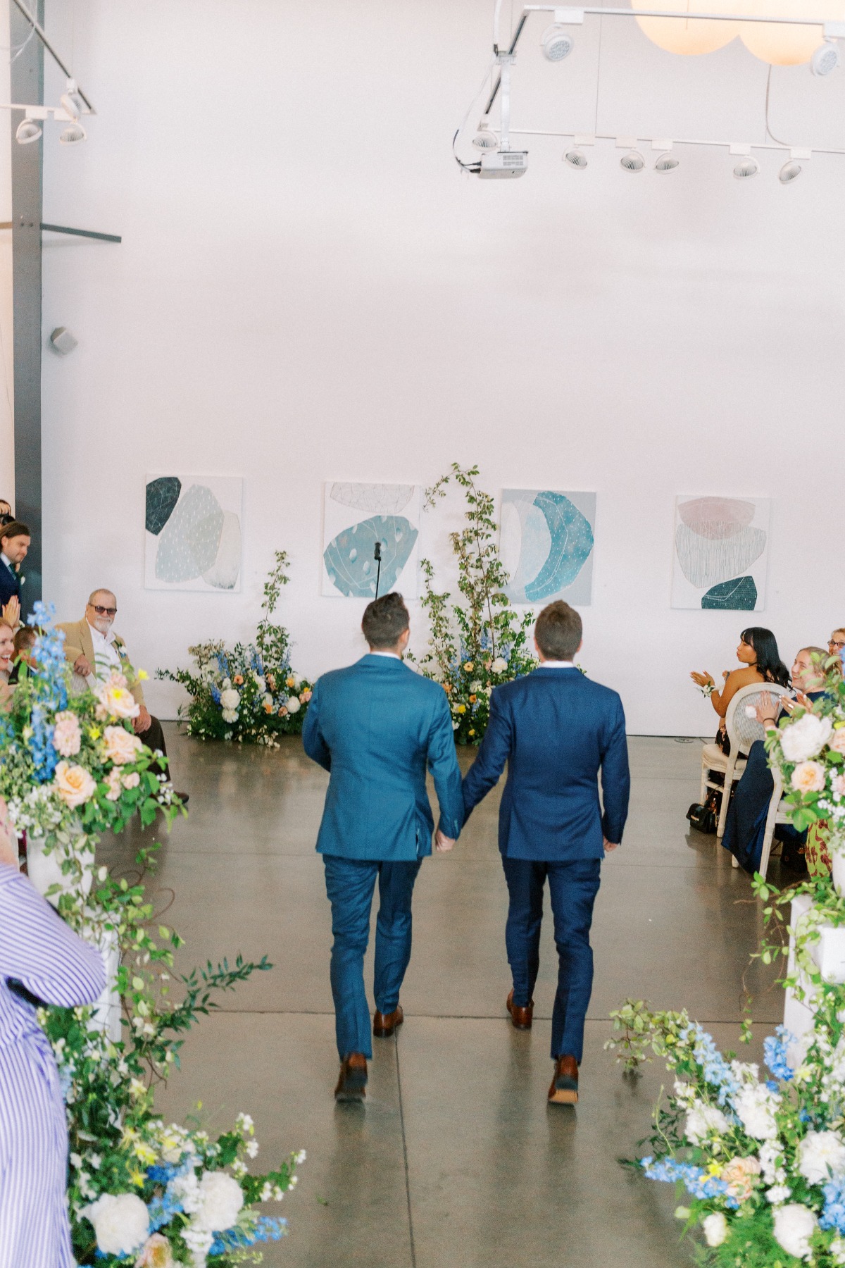 Two grooms walking into modern art gallery ceremony 