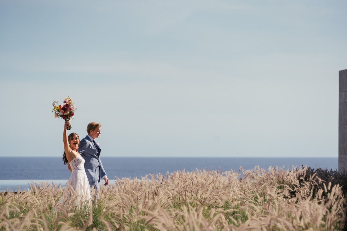 couple walking through field of grass overlooking the ocean