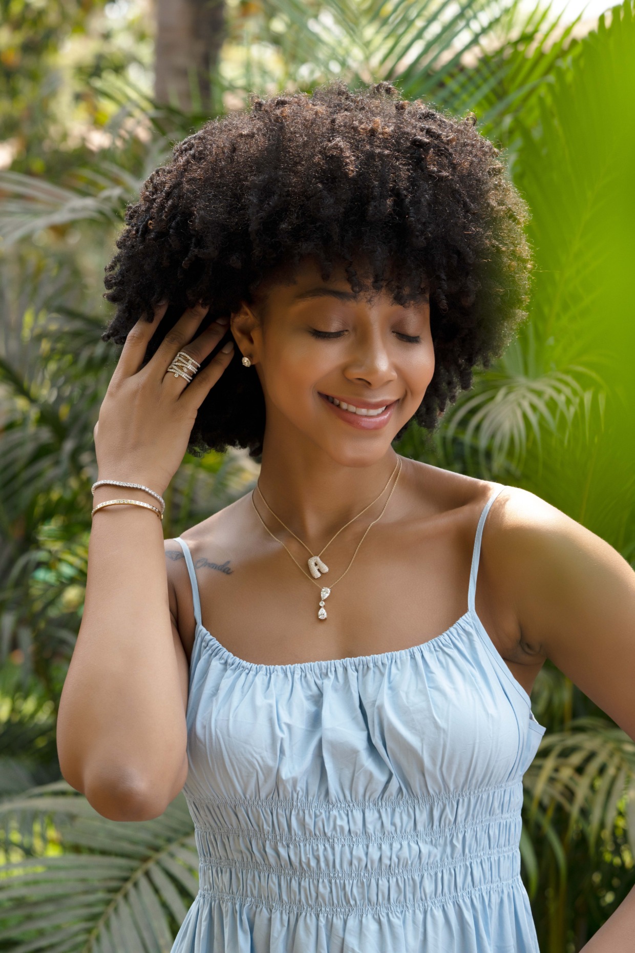 girl holding back hair outside next to green bush with lab grown diamond initial necklace