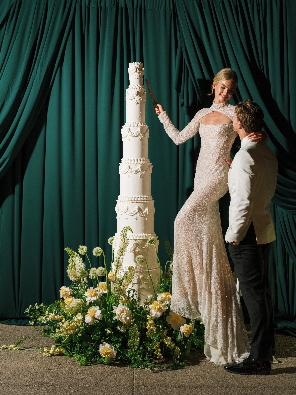 bride and groom standing on stool to reach huge towering white wedding cake
