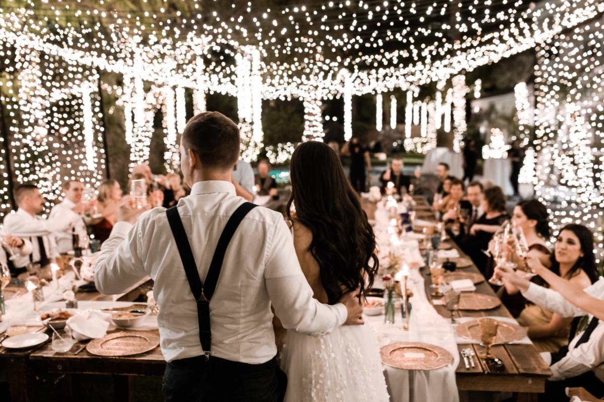 couple standing in front of string lit reception table