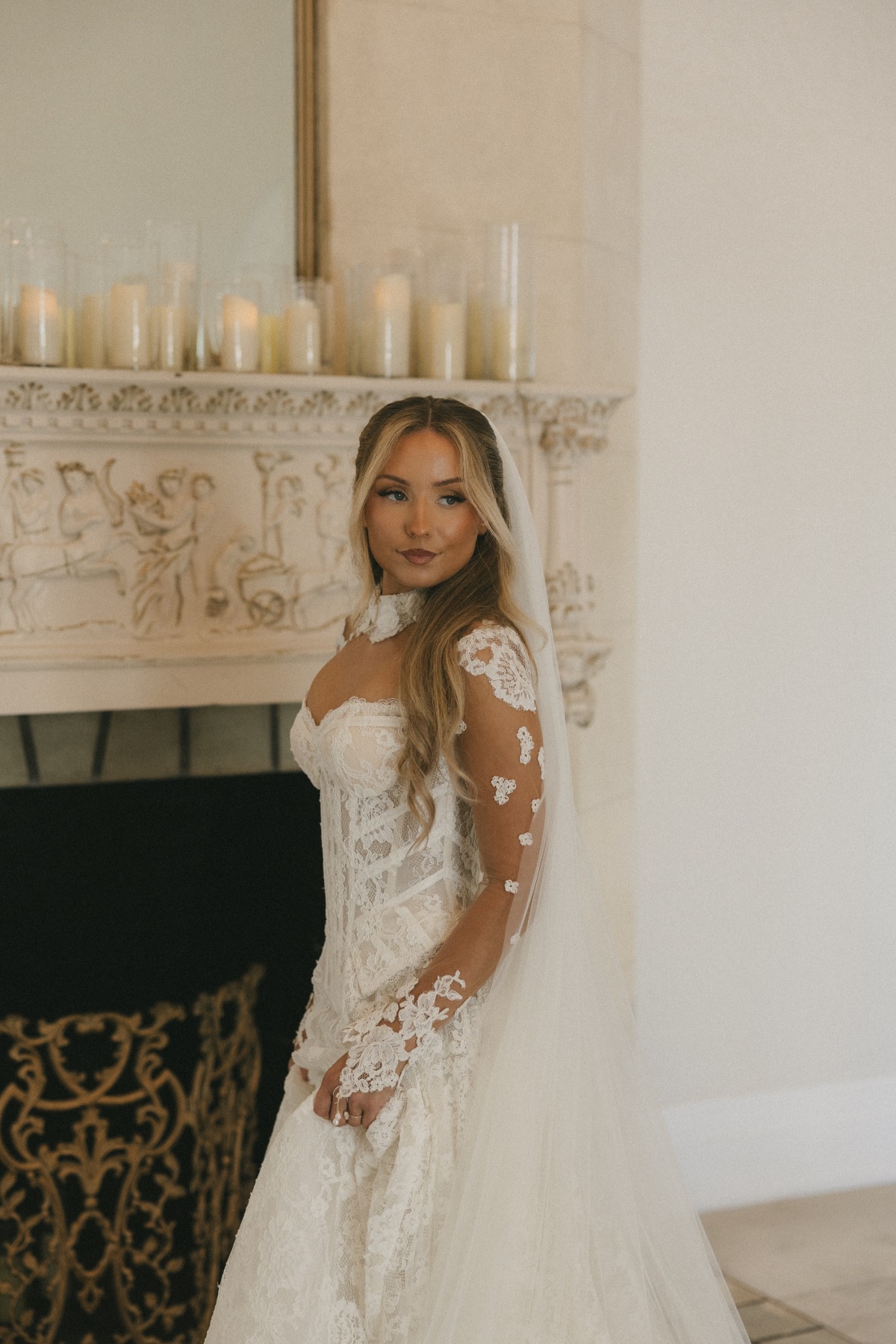 Slavic bride in front of vintage fire place in long sleeve lace sexy wedding gown and veil in hair