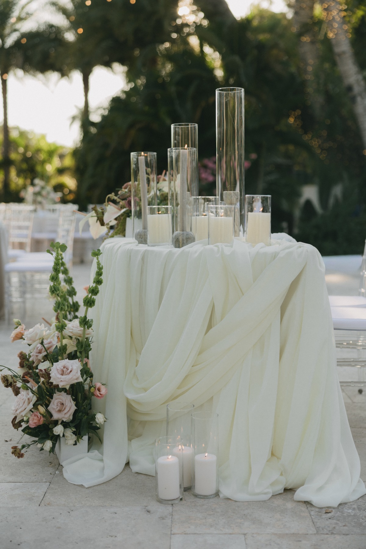 wedding cocktail table draped in ivory tulle and adorned with hurricane candles and florals
