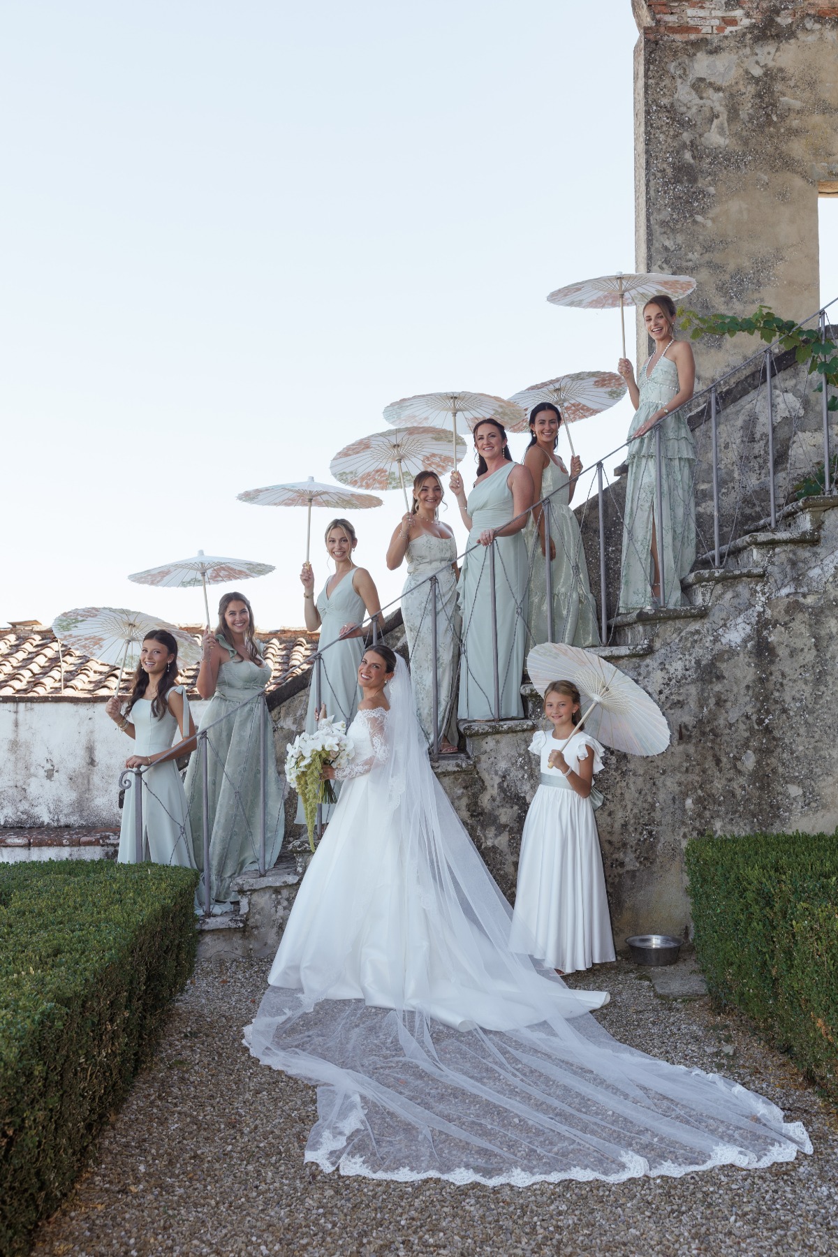 bride and bridesmaids standing on stairs of a castle holding their white umbrellas